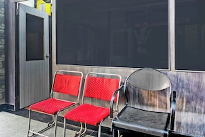 A row of metal chairs with red cushions, a black mesh chair, and a metal door with a glass panel. - Hotel O Anuguna Tulasi Grand (Hyderabad)