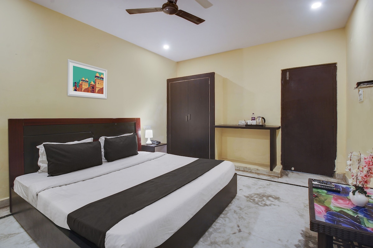 A hotel room with a bed, a nightstand, a desk, a ceiling fan, and a painting on the wall.