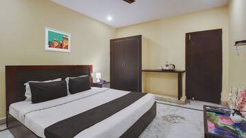 A hotel room with a bed, a nightstand, a desk, a ceiling fan, and a painting on the wall.