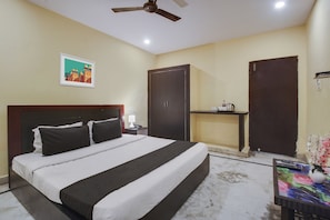 A hotel room with a bed, a nightstand, a desk, a ceiling fan, and a painting on the wall. - Hotel O Anuguna Tulasi Grand (Hyderabad)