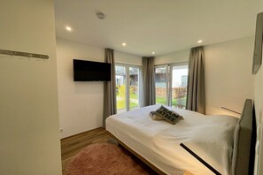 A bedroom with a bed, a flat-screen TV mounted on the wall, and a sliding glass door leading to a balcony. - Holiday apartment with 1 bedroom (Zingst)