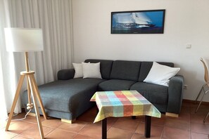 A living room with a sofa, a small table with a colorful tablecloth, a floor lamp, and a framed picture on the wall. - Apartment on the west side (Gager)