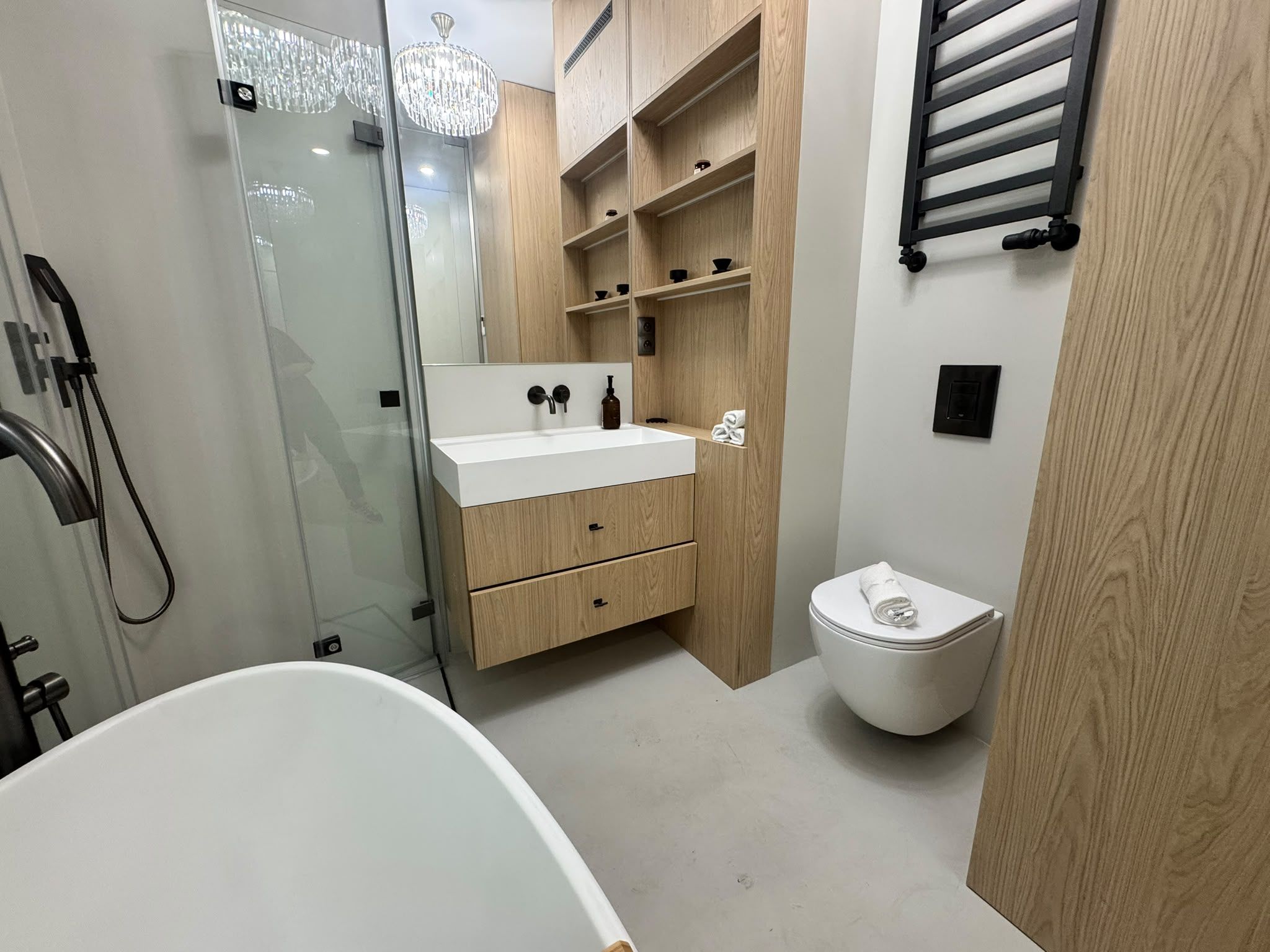 A modern bathroom with a freestanding bathtub, a glass-enclosed shower, and a wooden vanity with a sink and storage drawers.