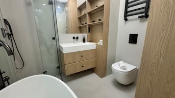 A modern bathroom with a freestanding bathtub, a glass-enclosed shower, and a wooden vanity with a sink and storage drawers.
