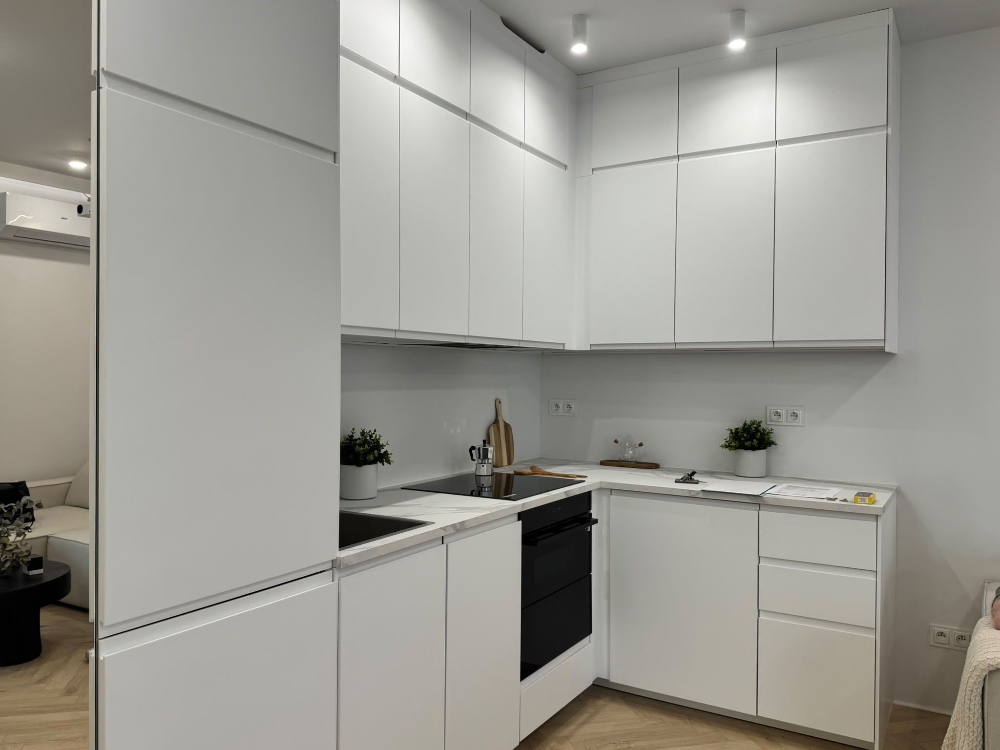 A modern kitchen with white cabinetry, a black dishwasher, and a countertop with a coffee maker and a plant.