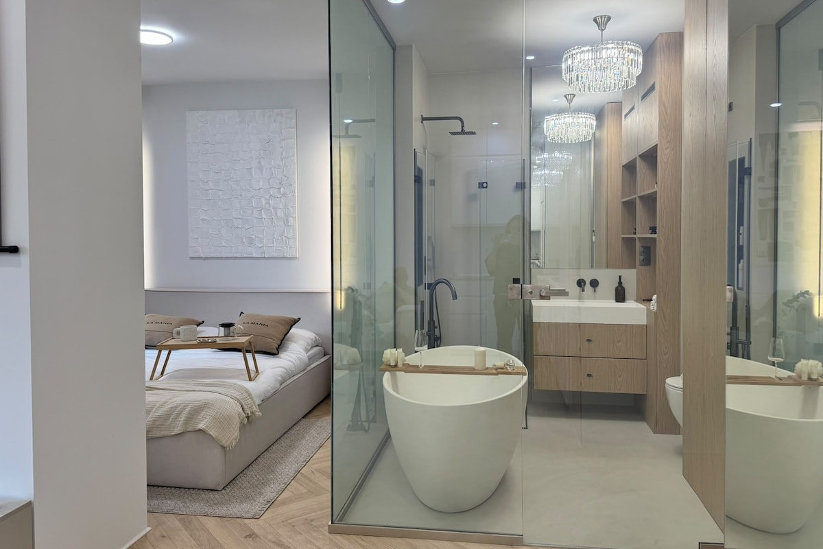 A modern bedroom with a large bed, bedside table, and a glass shower enclosure.