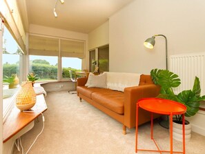 A modern living room with a leather sofa, a small orange table, and a potted plant.