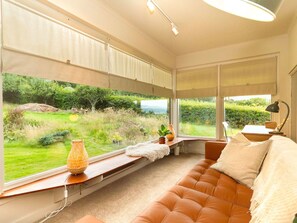A room with a large window, a sofa, a lamp, and a small table with a plant.