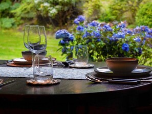Ein Tisch ist mit klarem Glas, Tellern und Schüsseln gedeckt, im Hintergrund ist ein Garten zu sehen.