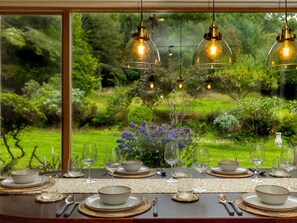 A dining table set with plates, bowls, and cutlery, with hanging light fixtures above.