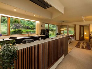 A modern kitchen with a wooden island, large windows, and a view of greenery.