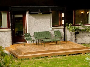 A wooden deck with a bench and two chairs, a textured wall, and a door.