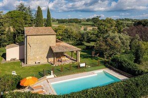 Eine Villa mit Swimmingpool, Sitzgelegenheiten im Freien und einer Steinstruktur.
