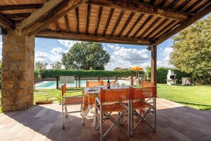 Eine Außenpatio mit Tisch und Stühlen, ein Pool im Hintergrund und ein überdachter Bereich mit Holzbalkendecke.