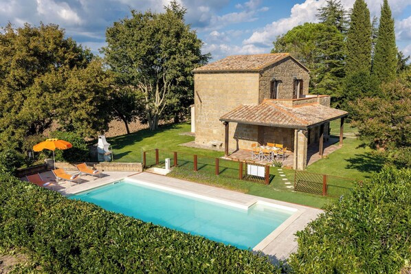Ein Steinhaus mit Pool, umgeben von viel Grün und einer eingezäunten Terrasse.