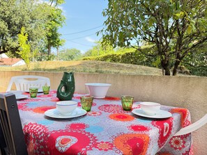 An outdoor dining area with a table set for two, surrounded by greenery and a clear sky. - New Listing (Royan)