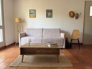 A living room with a sofa, a coffee table, a lamp, and two framed pictures on the wall. - New Listing (Royan)