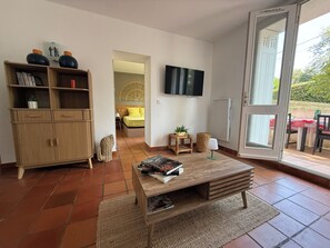 A modern living room with a wooden coffee table, a bookshelf, a flat-screen TV, and a view of the outdoors through a glass door. - New Listing (Royan)