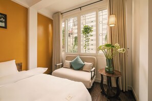 Ein Hotelzimmer mit Bett, einer Couch, einem kleinen Tisch mit Blumenvase und einem fenster mit Vorhängen.