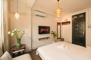 Ein Hotelzimmer mit einem Bett, einem Fernseher mit Netflix-Logo, einer Vase mit Blumen, einer Pendelleuchte und einer Tür.