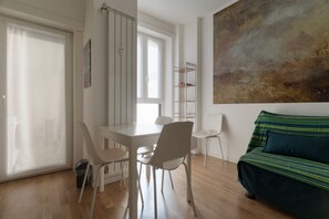 Ein Zimmer mit Esstisch, Stühlen, einer Couch, einem Bild an der Wand und einem Fenster mit Vorhängen.