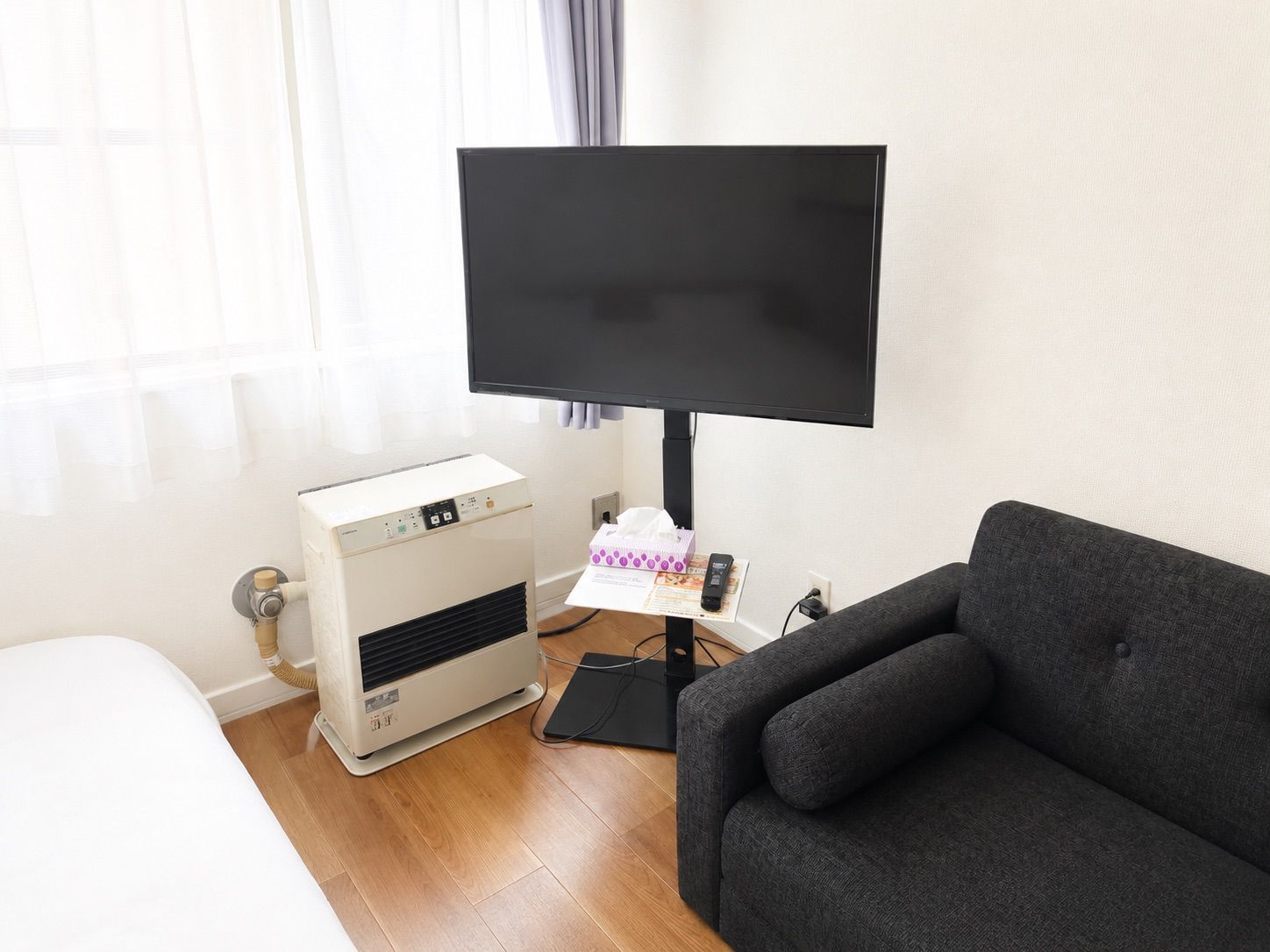 Een kamer met een bed, een verwarming, een flatscreen-tv en een grijze bank.