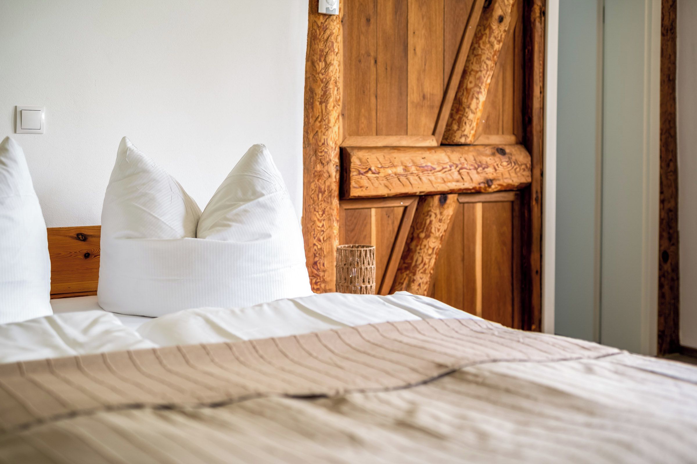 Ein ordentlich bezogenes Bett mit gestreifter Tagesdecke, einem Holz-Kopfstück und einem weißen Kopfkissen.