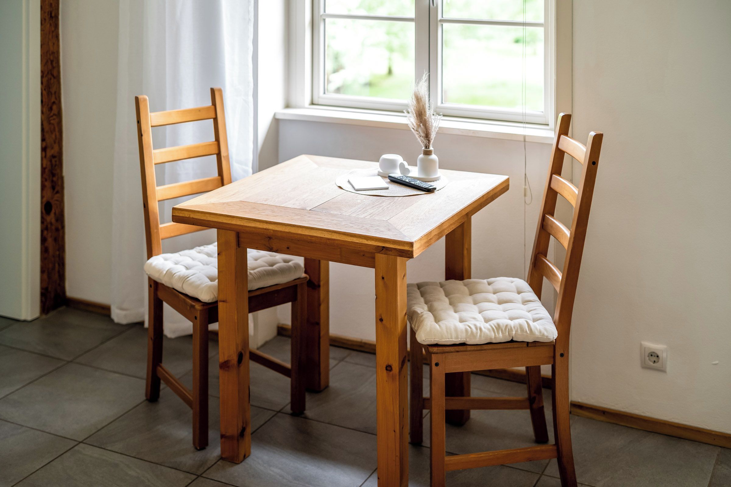 Ein Holztisch mit zwei Stühlen, einer Fernbedienung und einer Vase mit getrockneten Blumen.