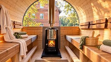 A sauna room with wooden benches, a central wood-burning stove, and a view through a semi-circular window.