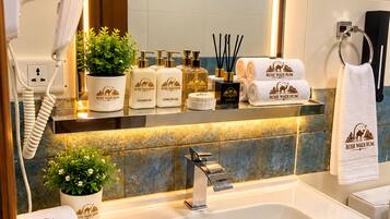 A bathroom with a sink, a hairdryer, a mirror, and toiletries branded with 'ROSE WADI RUM'.