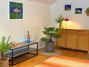 A room with a wooden floor, a dining table with chairs, a potted plant, a cabinet, and framed artwork on the wall.