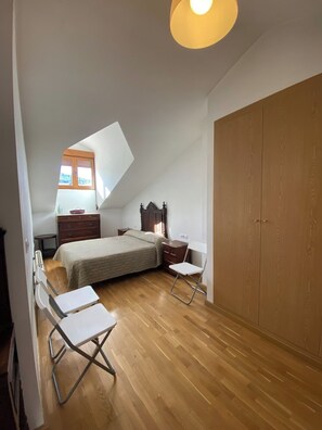 A bedroom with a sloped ceiling, a bed, a wardrobe, a desk, and a chair.