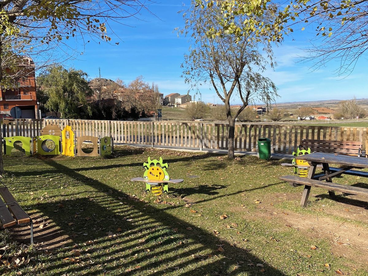 Een park met een speeltuin, picknicktafels en een houten omheining.