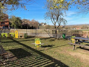 A park with a playground, picnic tables, and a wooden fence.