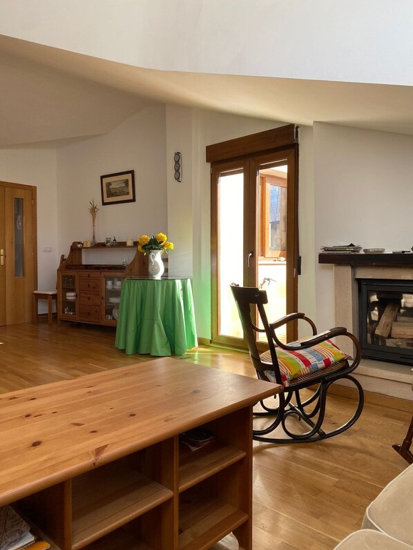 A room with a wooden table, a rocking chair, a fireplace, and a green tablecloth.