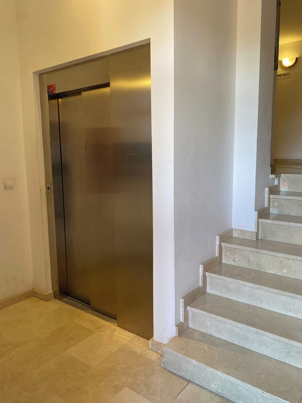 Een moderne lift met een metalen afwerking, naast een trap met beige treden.