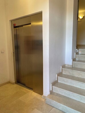 A modern elevator with a metallic finish, adjacent to a staircase with beige steps.