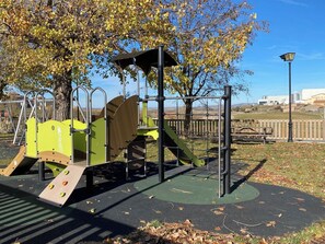 A playground with climbing structures and a slide, surrounded by trees and a clear sky.