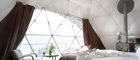 A cozy tented room with a bed, a chair, a small table with a plant, and a heater.