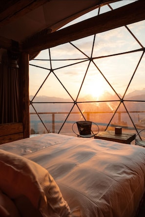 Una habitación acogedora con un ventanal grande, una cama y una mesa con una silla.