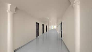 Un largo y estrecho pasillo con paredes blancas y piso de baldosas, que conduce a varias puertas.