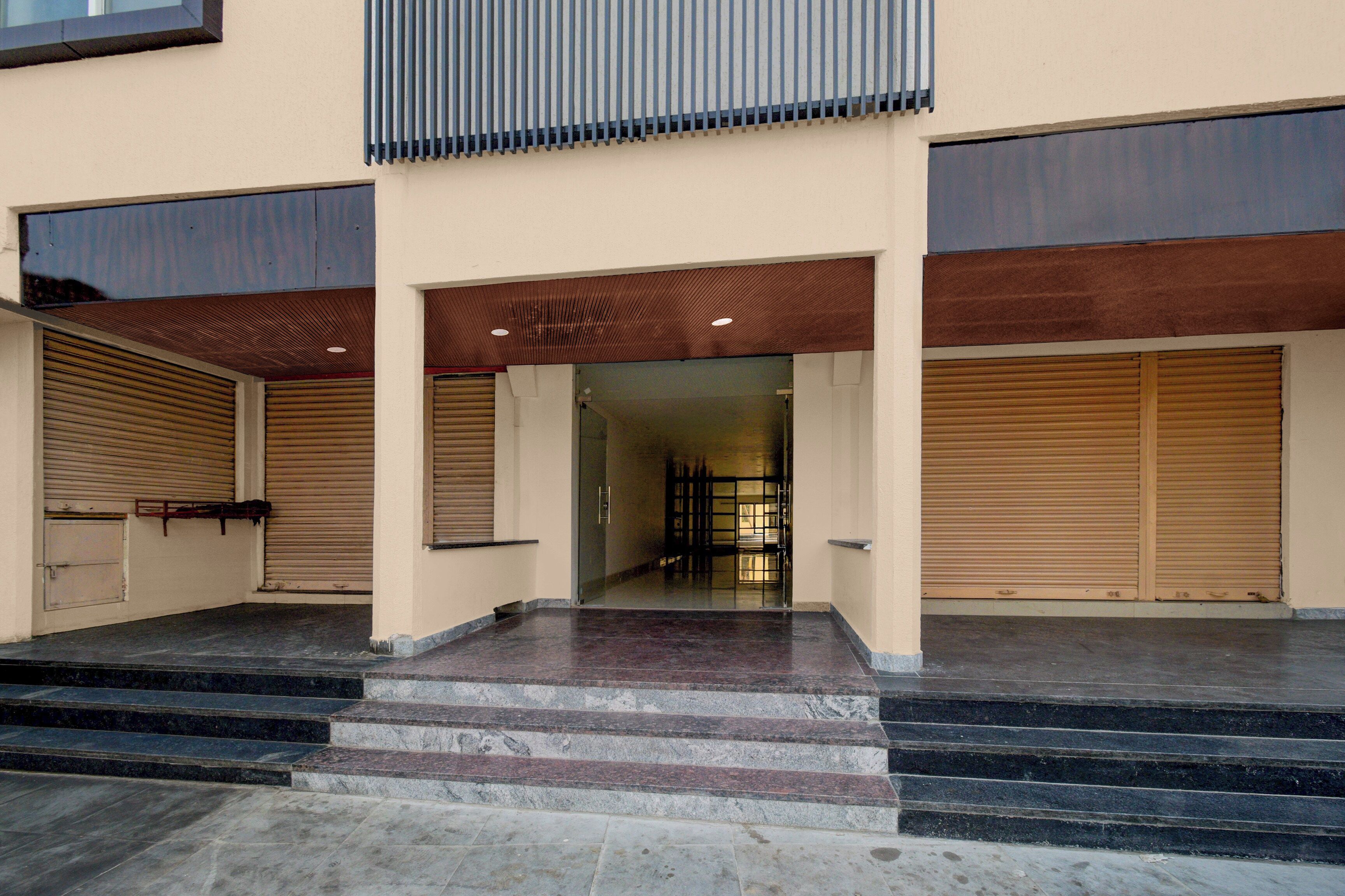 A building entrance with a set of stairs leading up to a door, flanked by two closed roller shutters.