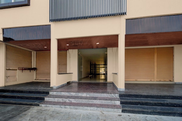 A building entrance with a set of stairs leading up to a door, flanked by two closed roller shutters.