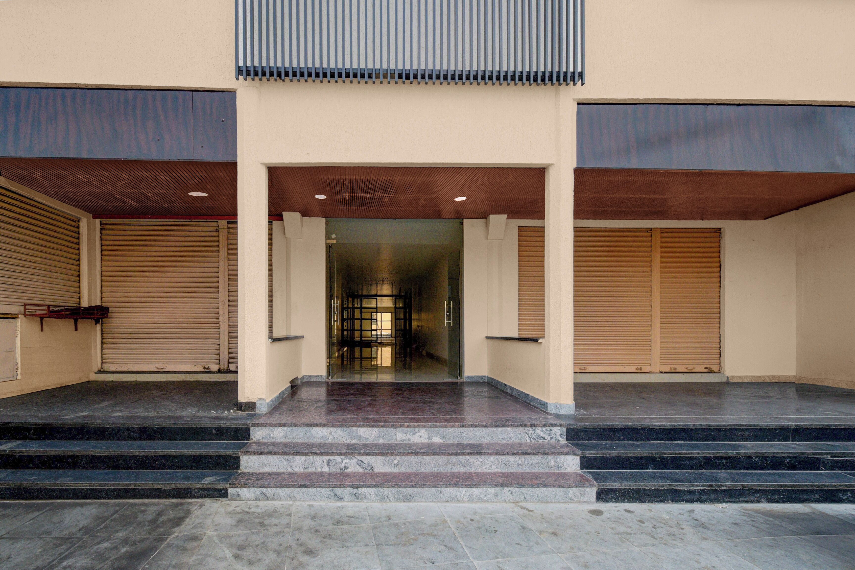 A building entrance with a set of stairs leading up to a door, flanked by two closed shuttered windows.