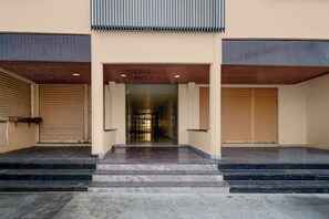 A building entrance with a set of stairs leading up to a door, flanked by two closed shuttered windows.