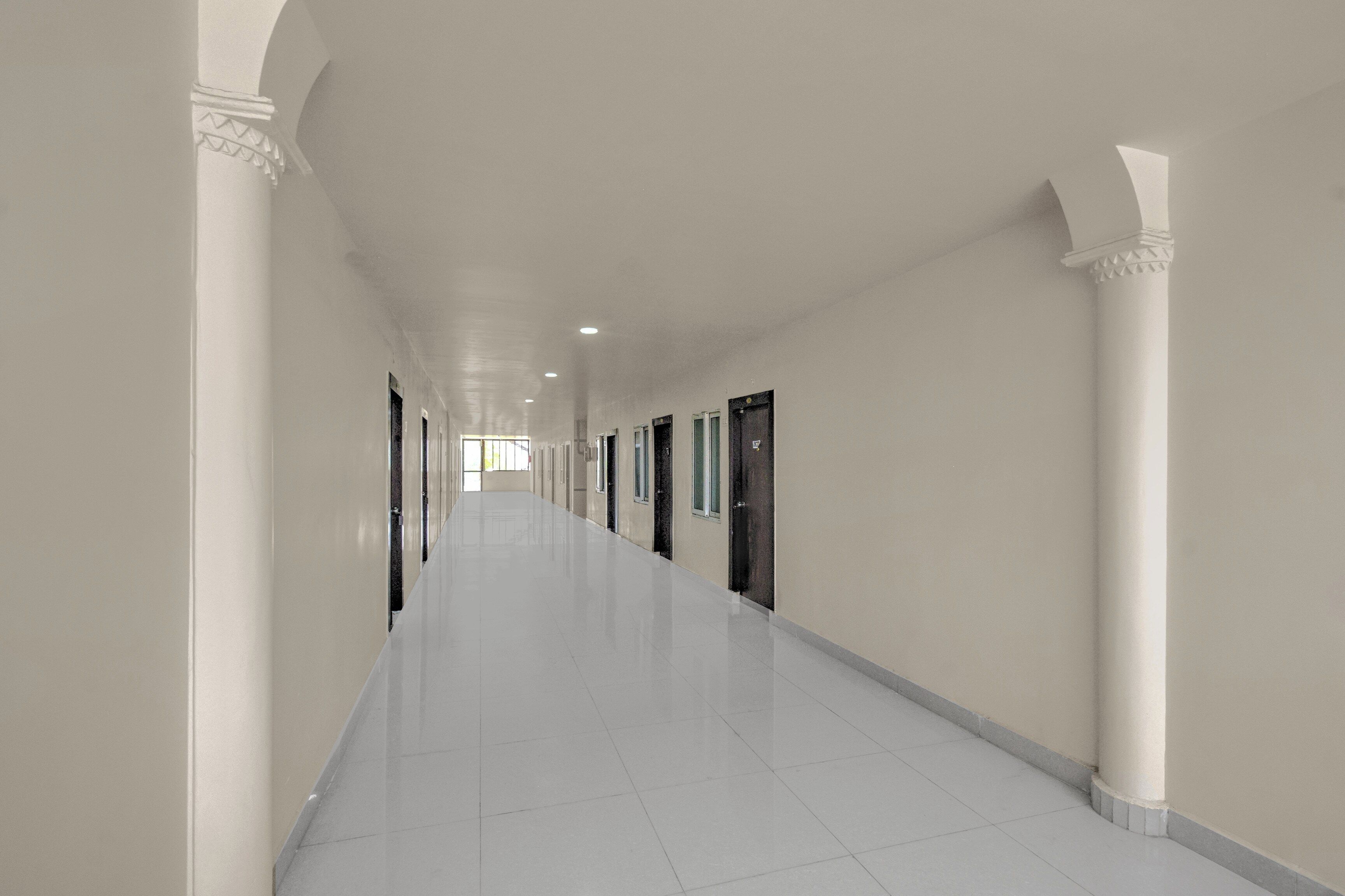 A long, narrow hallway with white walls and a tiled floor, leading to multiple doors.