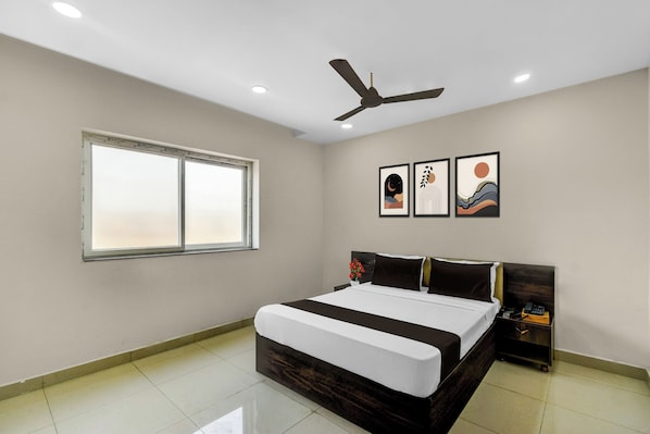 Une chambre à coucher avec un lit, un ventilateur de plafond, une fenêtre et trois œuvres d’art encadrées accrochées au mur.