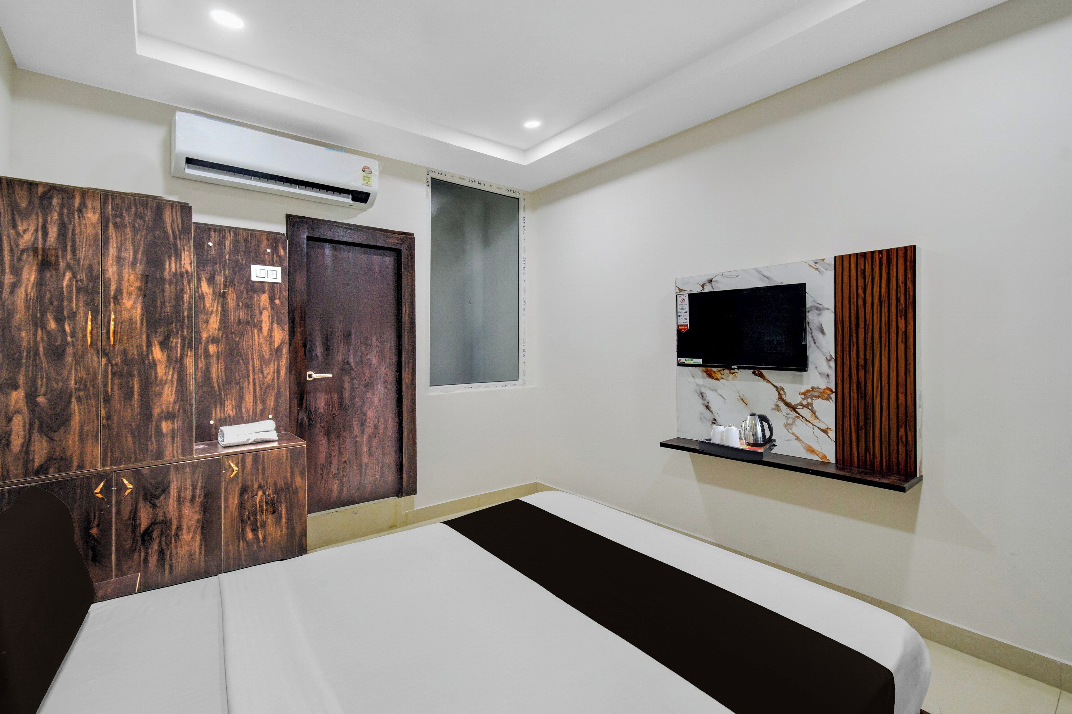 A hotel room with a bed, a wardrobe, a television mounted on the wall, and a small shelf with items.