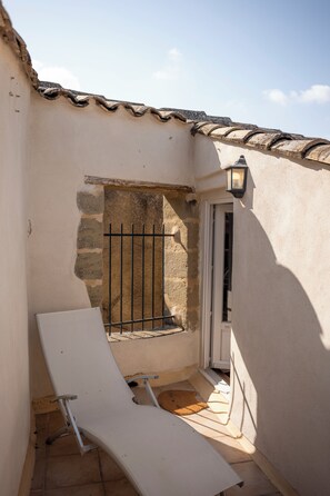 Un petit espace extérieur avec une chaise blanche, une porte et un mur surmonté d’un toit en tuiles.