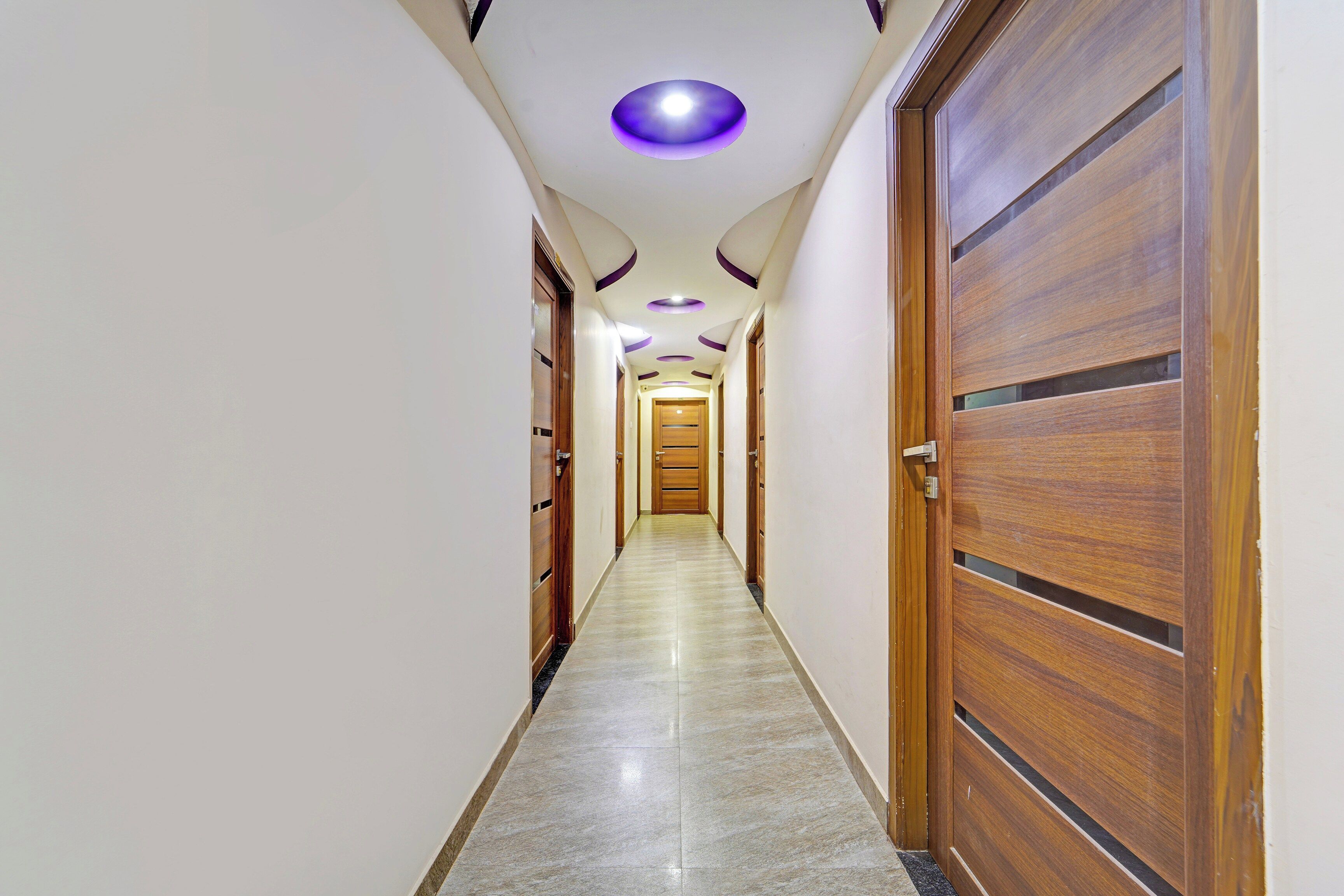 A hallway with wooden doors, a marble floor, and recessed lighting.